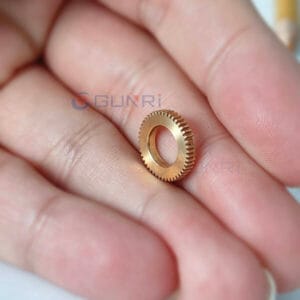 Micro brass knurled gear ring held between fingers showing miniature precision scale