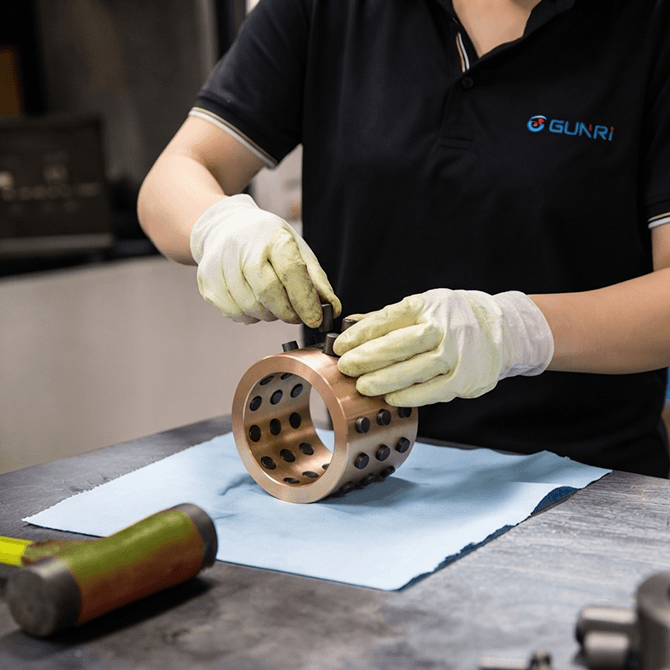 factory worker assembling self-lubricating bronze construction bearing with graphite plugs, precision machined brass bushing in industrial workshop, self-lubricating construction bearings manufacturing process